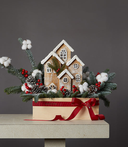Snowy village Christmas centerpiece with miniature wooden houses, frosted evergreens, and red berries in wooden box