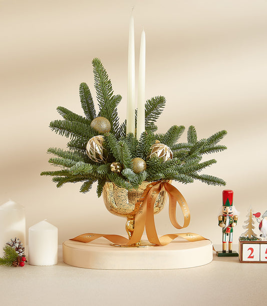 Golden Christmas centerpiece with fir branches, white taper candles, and gold ornaments in textured glass bowl