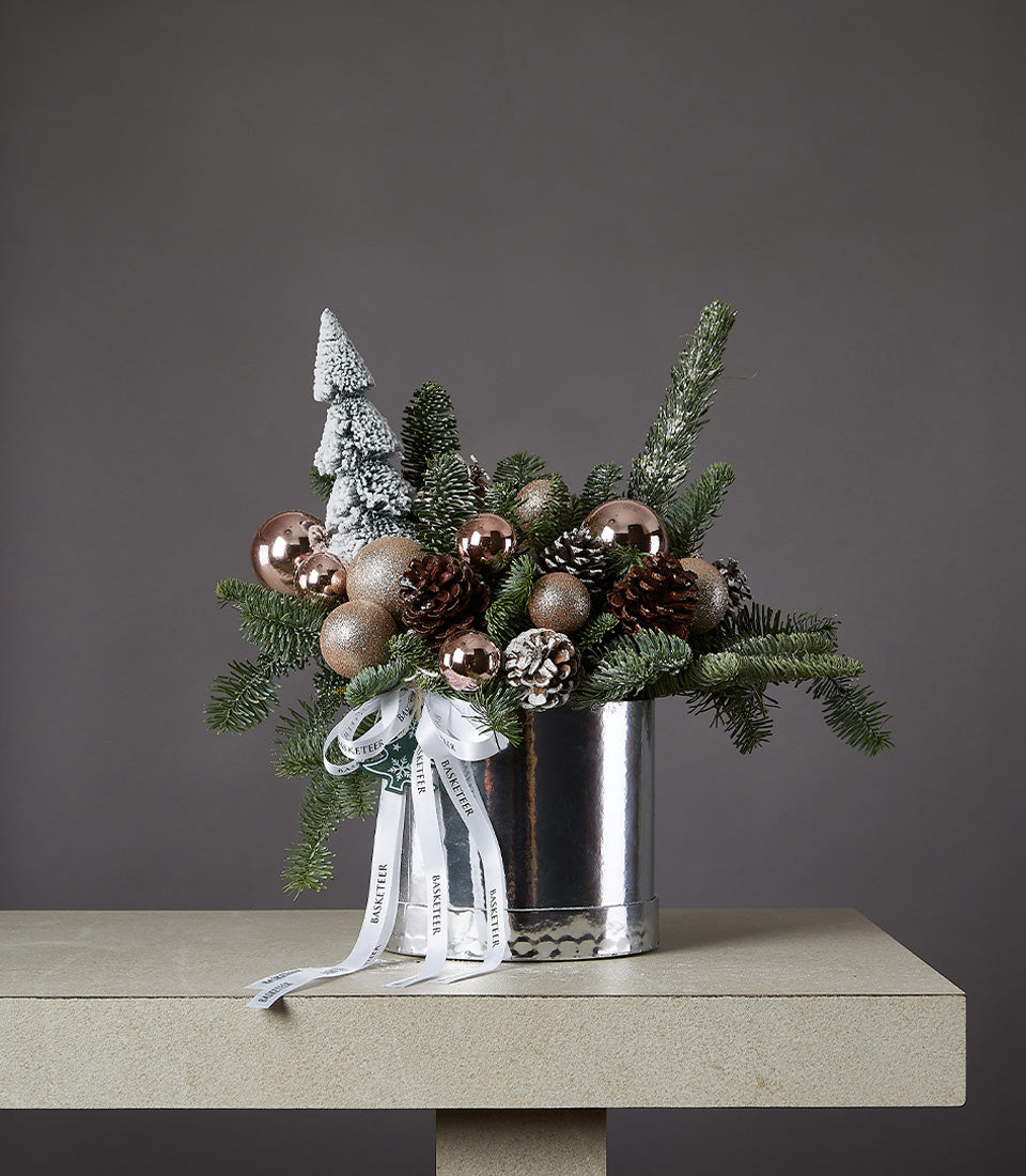 Frosted pine Christmas arrangement with rose gold ornaments and pinecones in silver hammered vase