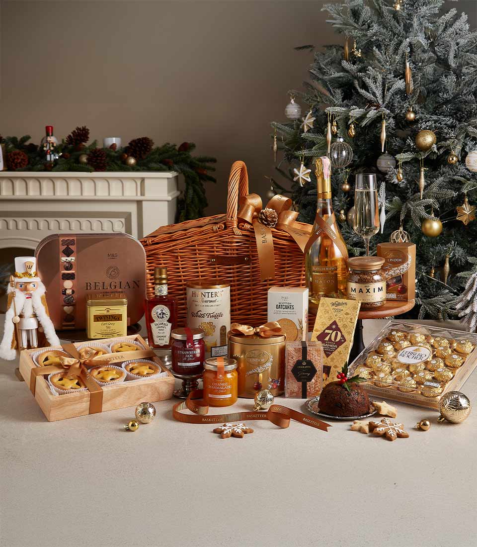 Luxe Christmas hamper with champagne, chocolates, jam, tea, pudding and mince pies in wicker basket with gold ribbon