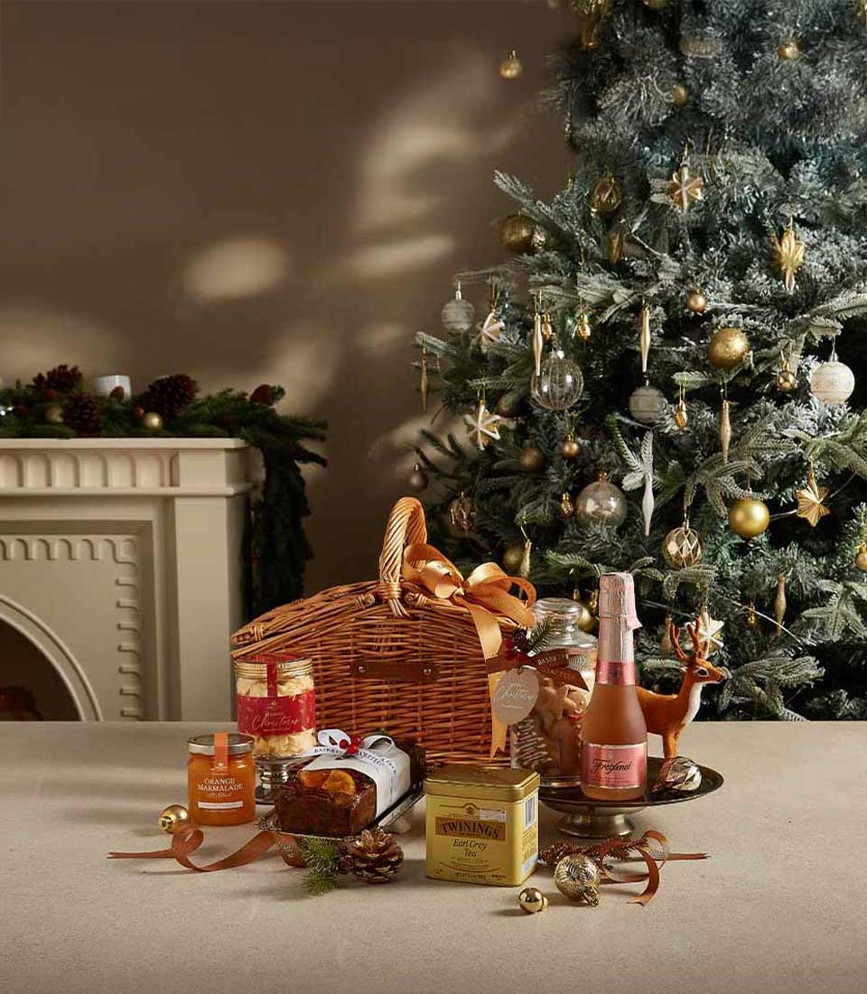 Luxury Christmas hamper with sparkling wine, Earl Grey tea, fruitcake, and marmalade in woven wicker basket with gold ribbon