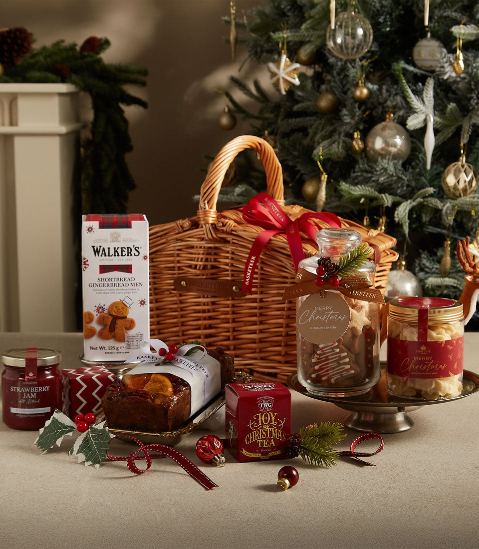 Woven wicker Christmas hamper with shortbread, gingerbread, jam, fruit cake, and festive tea, tied with red ribbon