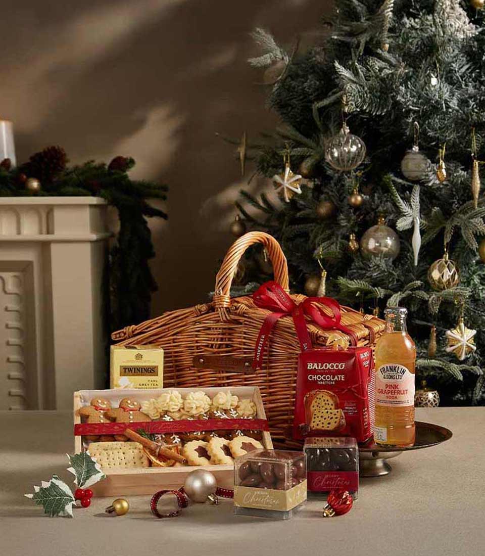 Woven wicker Christmas hamper with red ribbon, gourmet treats, tea, cookies, and chocolate-covered nuts