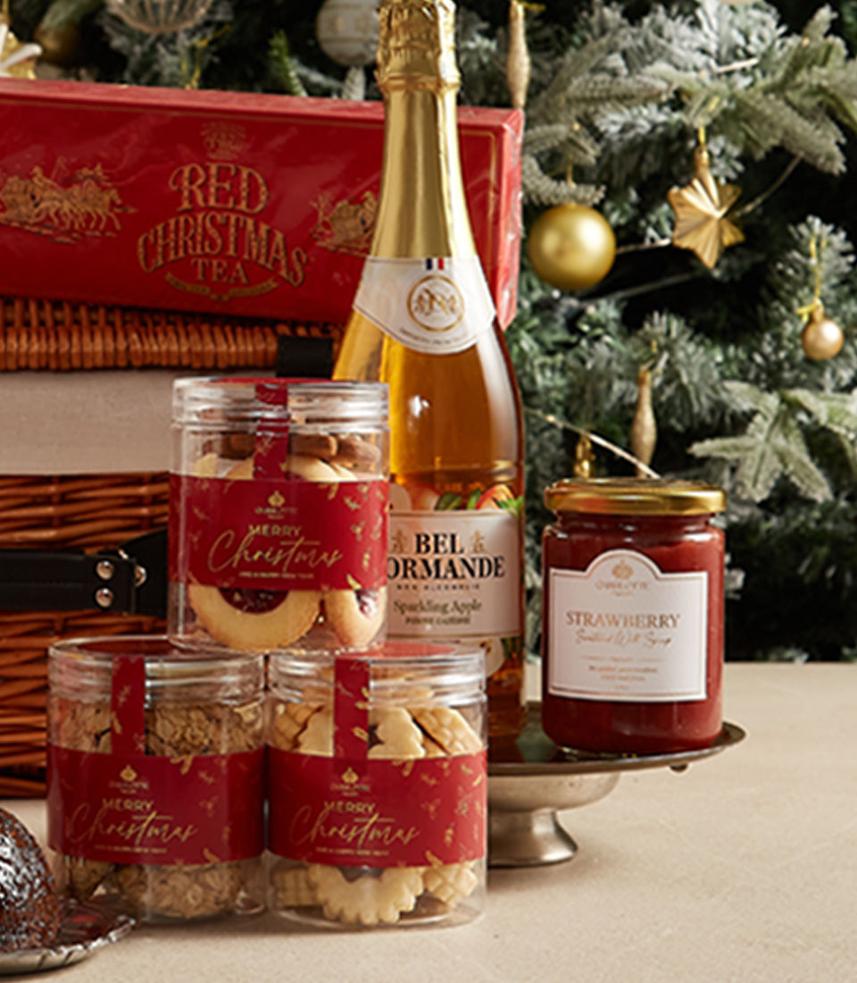Festive Christmas hamper with assorted cookies, sparkling apple cider, red tea tin, and strawberry jam in wicker basket