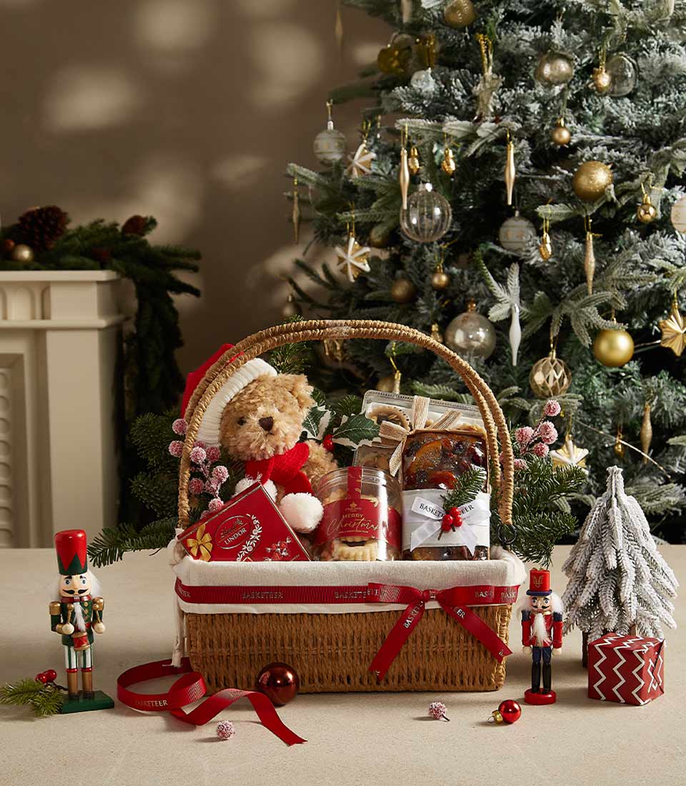 Festive Christmas hamper with teddy bear, Lindor chocolates, cookies, and fruitcake in woven basket with red ribbon