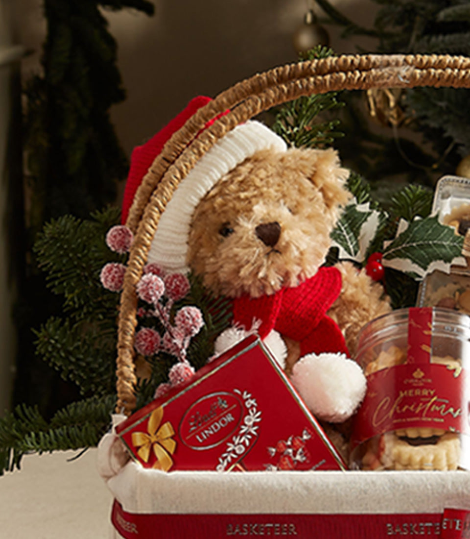 Festive teddy bear with red Santa hat, Lindor chocolates, and Christmas cookies in luxury holiday gift basket