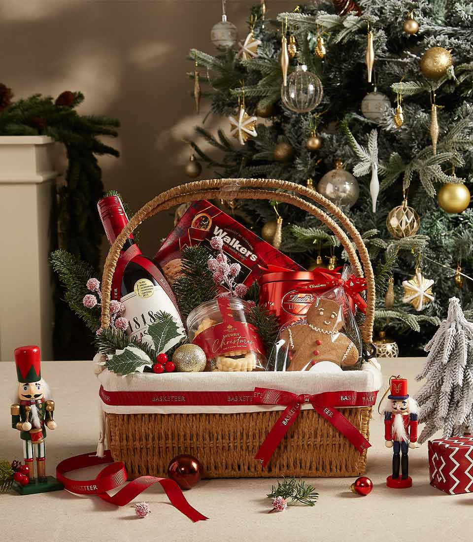 Festive wicker Christmas gift basket with sparkling wine, shortbread, cookies, and gingerbread, adorned with red ribbon and