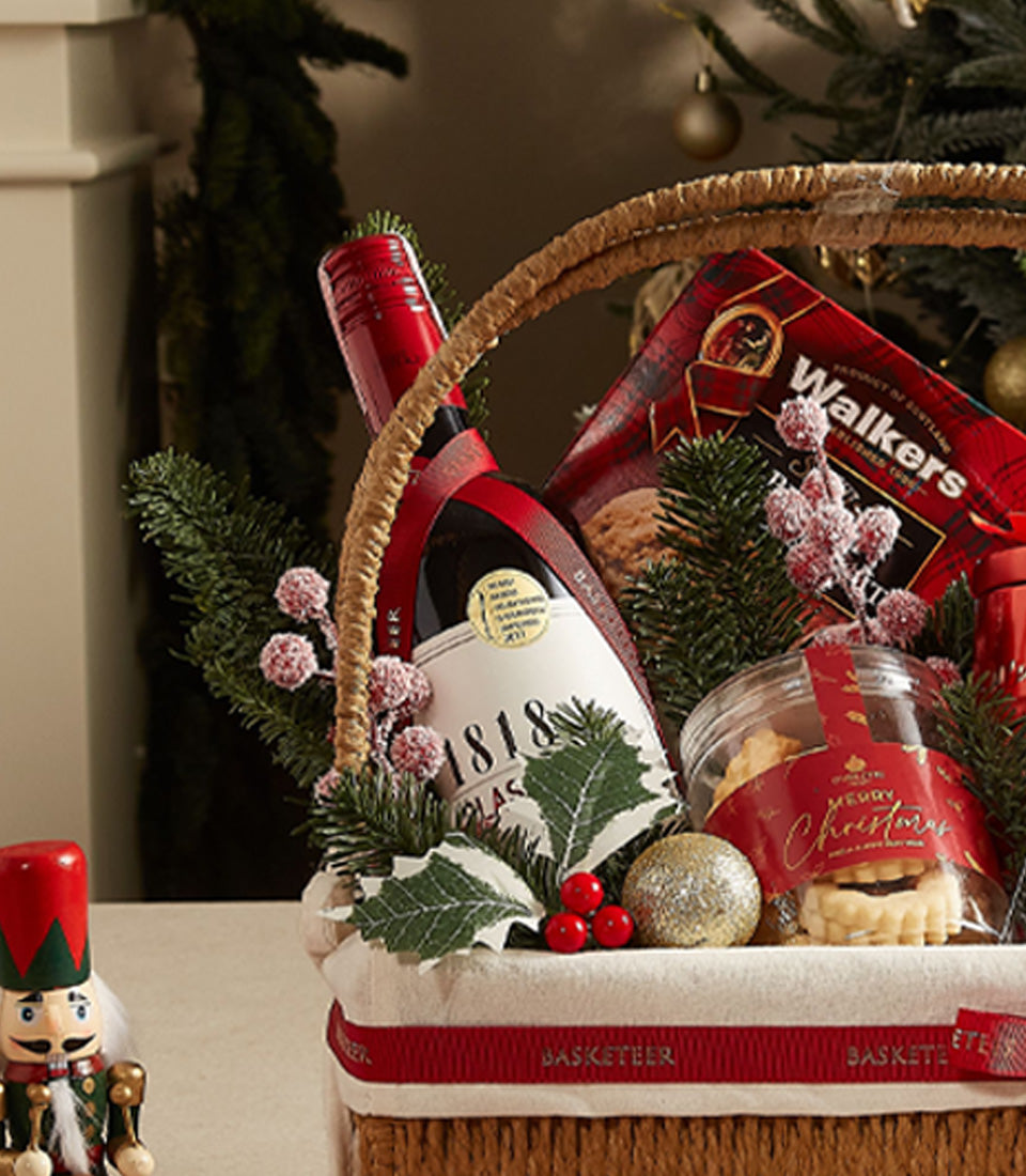 Premium red wine Christmas hamper with shortbread, festive cookies, pine branches, and gold ornaments in woven basket
