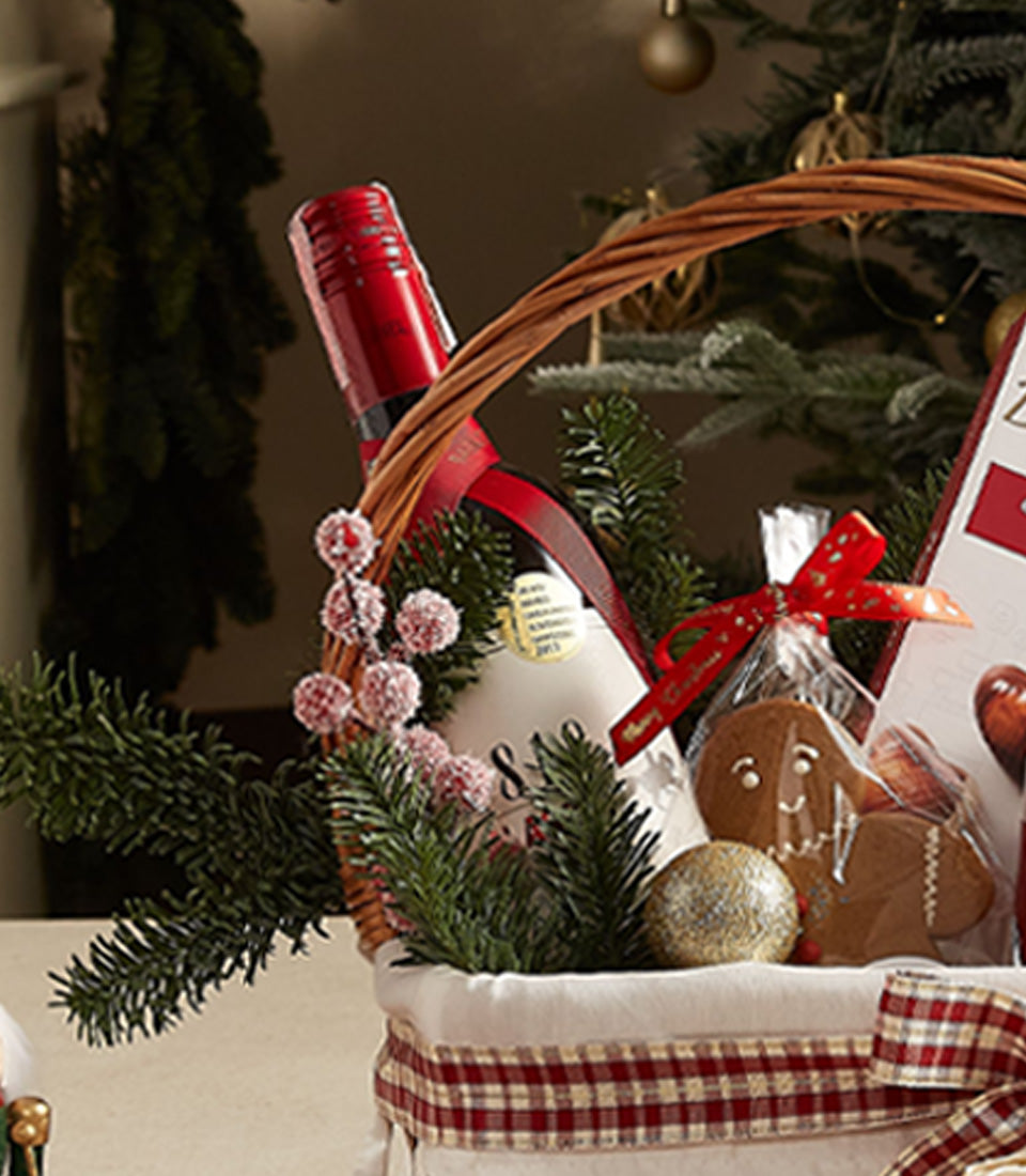 Woven brown Christmas gift basket with red wine, gingerbread cookie, frosted berries and plaid ribbon