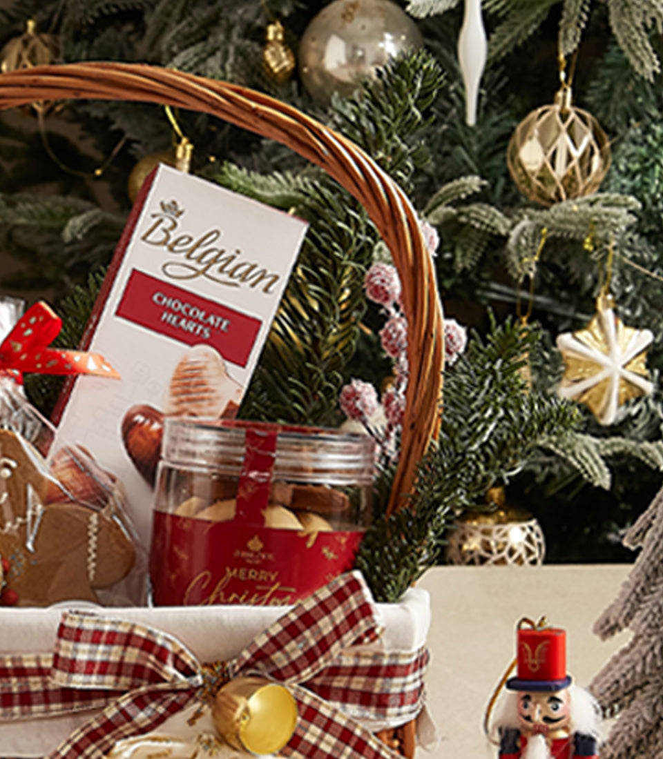 Festive wicker gift basket with Belgian chocolates, holiday cookies, gingerbread, and red plaid ribbon for Christmas