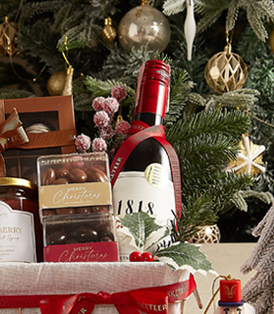 Elegant Christmas wine gift hamper with red wine, chocolate-covered nuts, and gourmet treats in festive basket