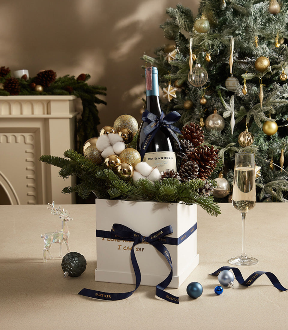 Luxury Christmas wine gift box with red wine, gold and blue ornaments, pine branches, and dark blue ribbon bow