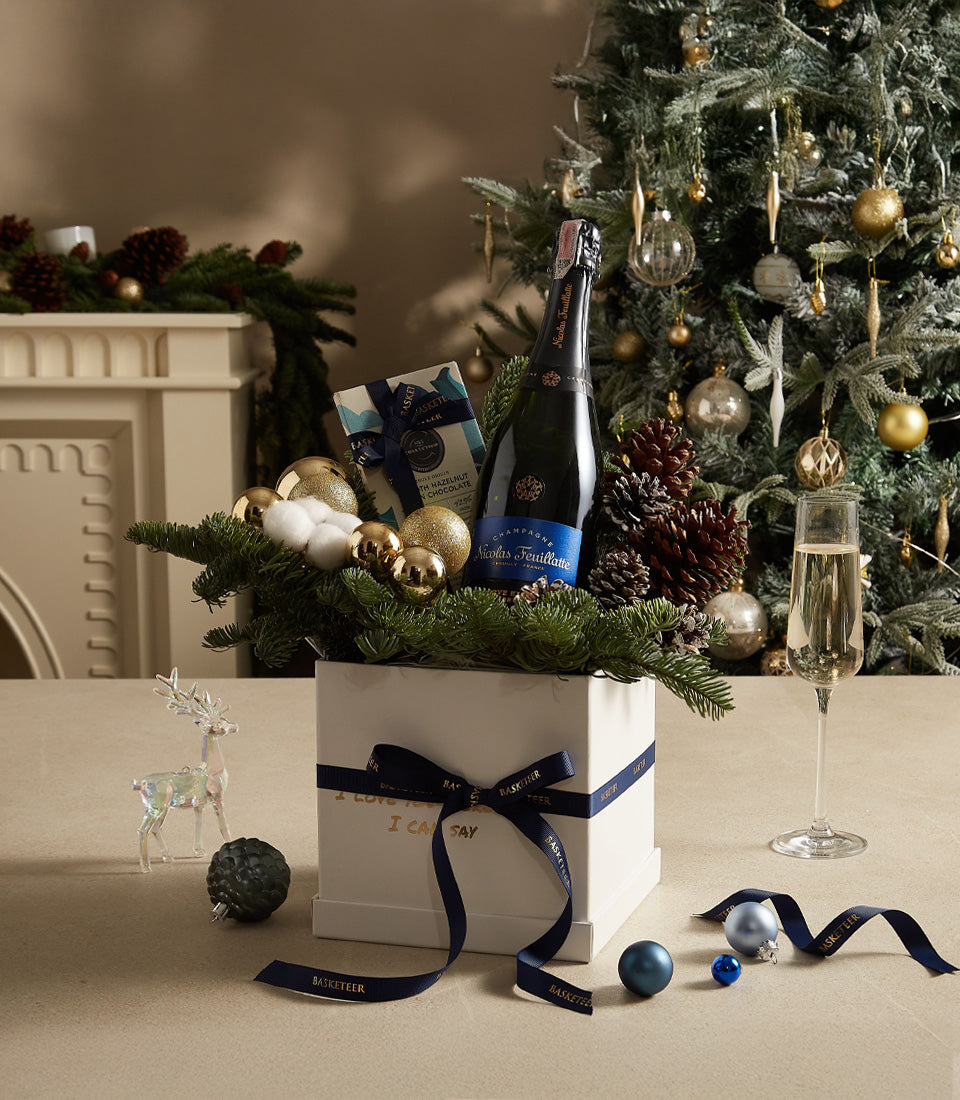 Elegant blue and gold Christmas gift box with champagne, chocolates, and festive greenery
