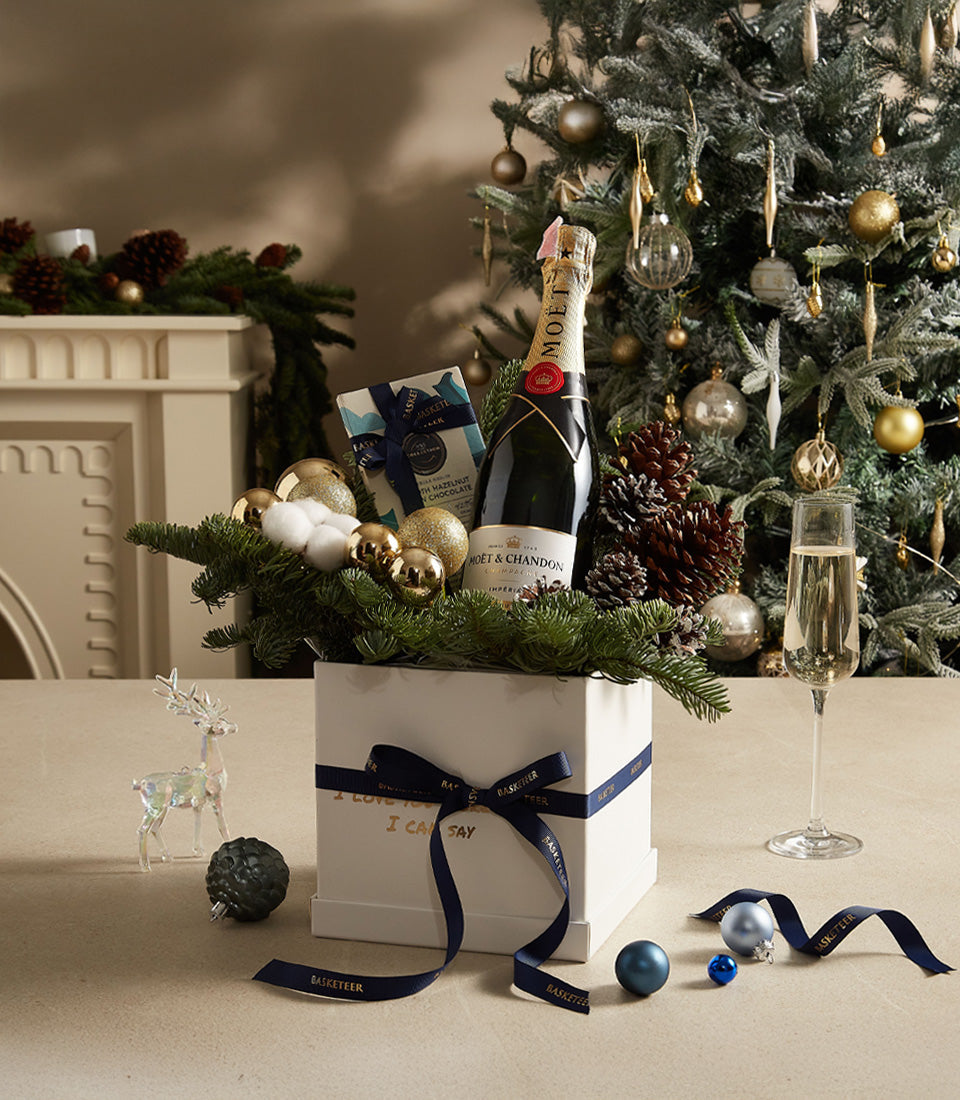 Luxury white gift box with champagne, chocolates, and gold ornaments tied with dark blue ribbon for Christmas