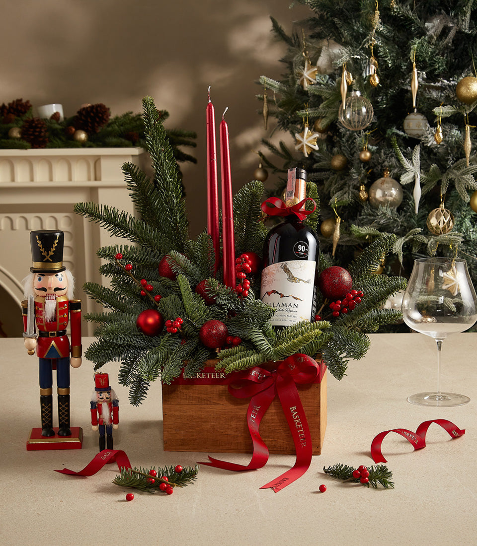 Festive red wine gift box with evergreen branches, berries, candles, and holiday decorations for Christmas