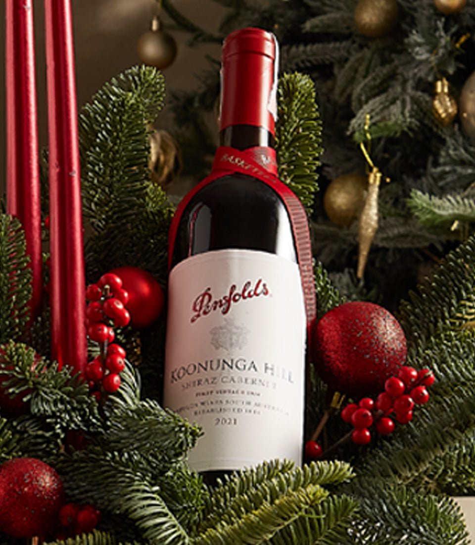 Penfolds red wine with festive pine, berries, and red ornaments in holiday gift arrangement