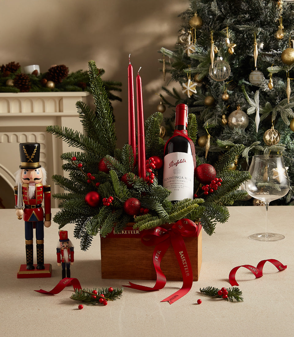 Festive red wine gift box with taper candles, fir branches, and Christmas nutcrackers, luxury hamper