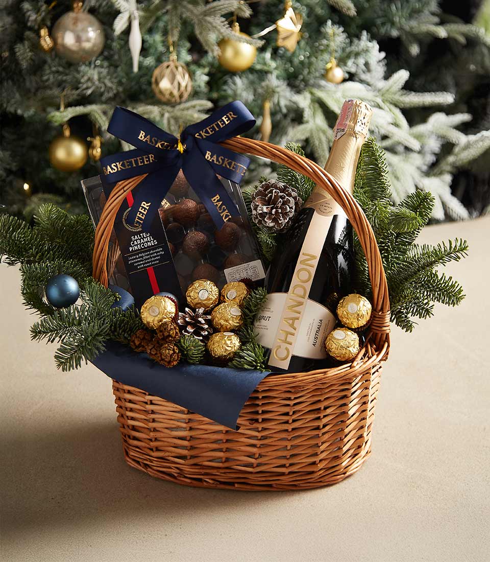 Premium champagne and chocolate gift basket with dark truffles, gold-wrapped pralines, and festive pine accents in woven