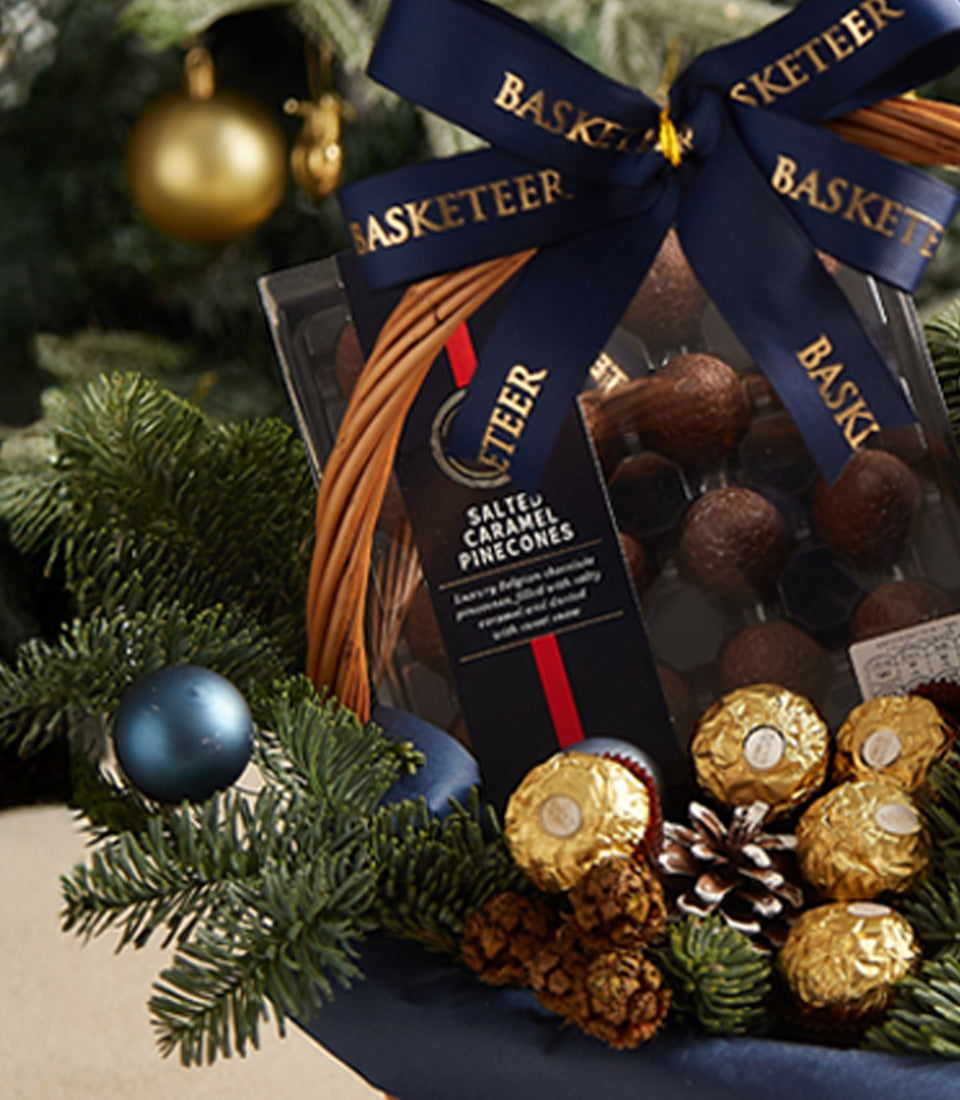 Festive wicker gift basket with champagne, salted caramel chocolate truffles, and gold ornaments for Christmas