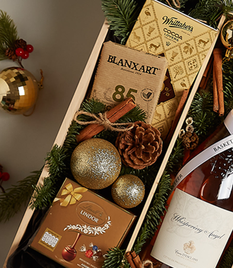 Festive rosé wine gift hamper with chocolate truffles, cinnamon sticks, and gold baubles in wooden box