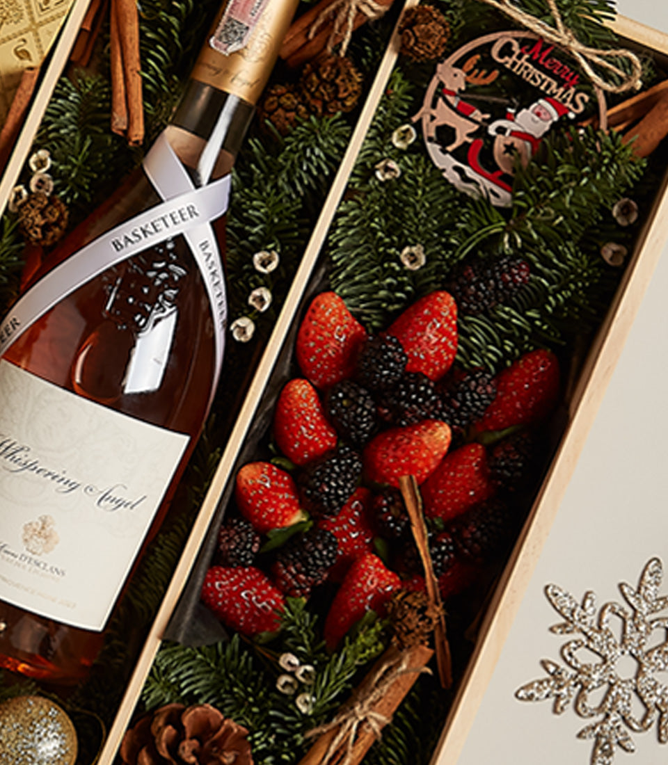 Rosé wine and fresh berries in festive wooden gift box with pine and golden ornaments for Christmas