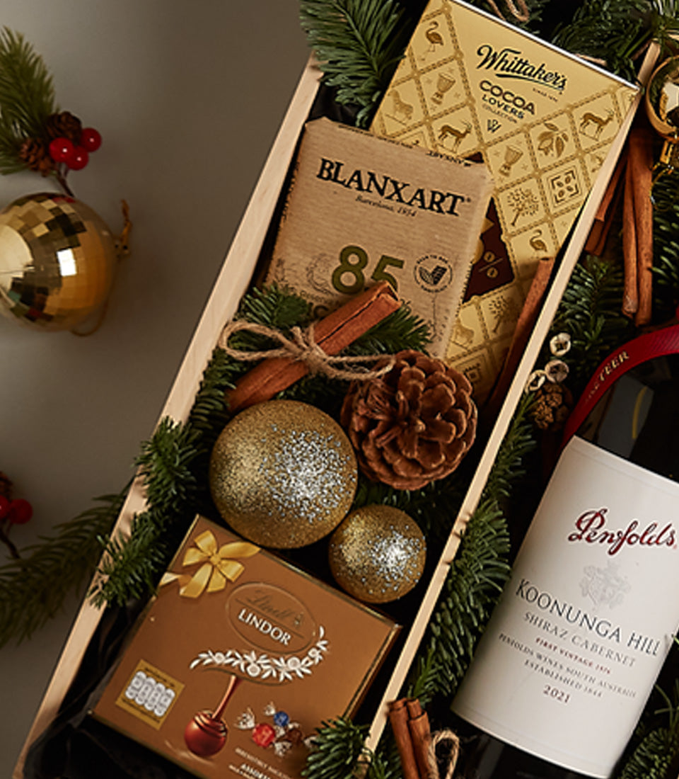 Festive red wine gift box with artisan chocolates, cinnamon, and gold Christmas baubles