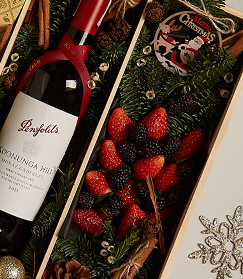 Festive wine gift box with Penfolds Shiraz Cabernet, fresh strawberries, blackberries, cinnamon, and Christmas ornament