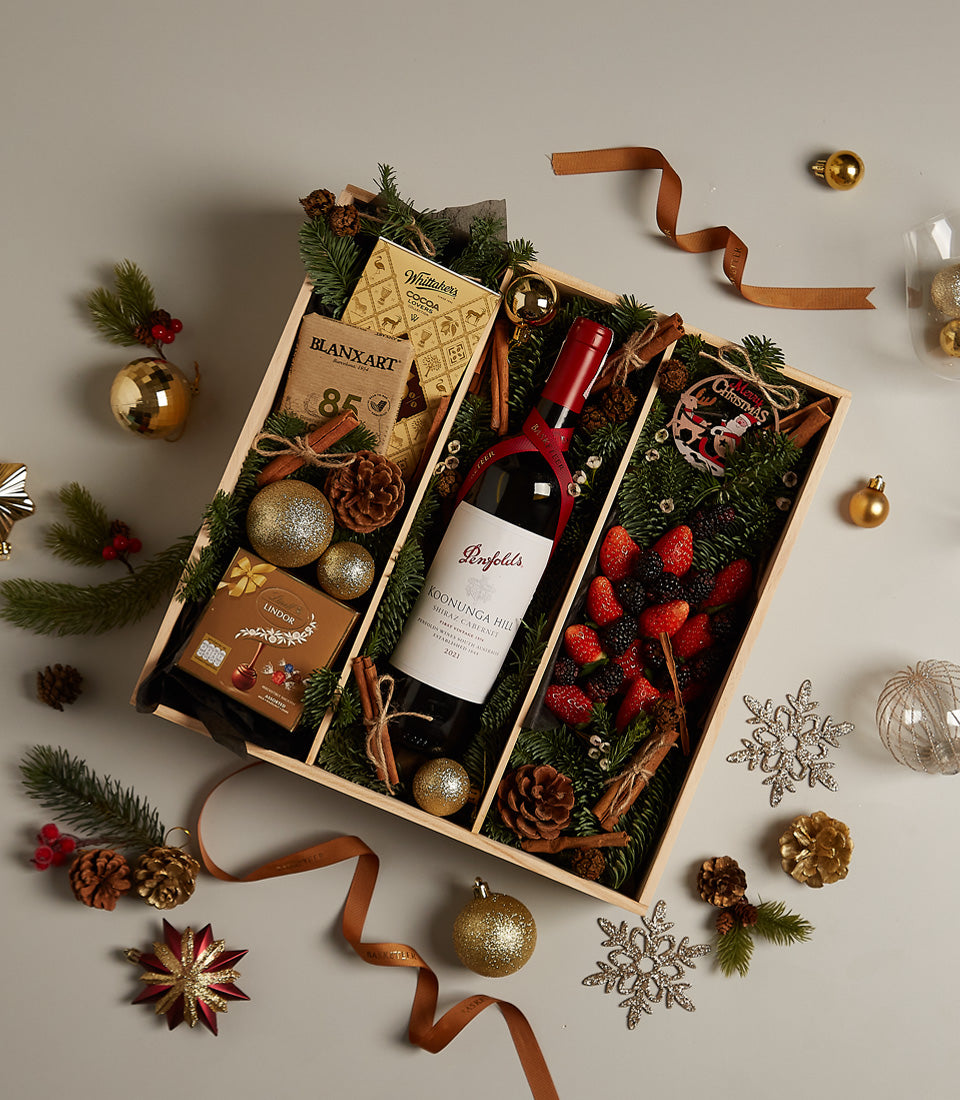 Festive wooden gift tray with red wine, fresh berries, gourmet chocolates, and holiday greenery