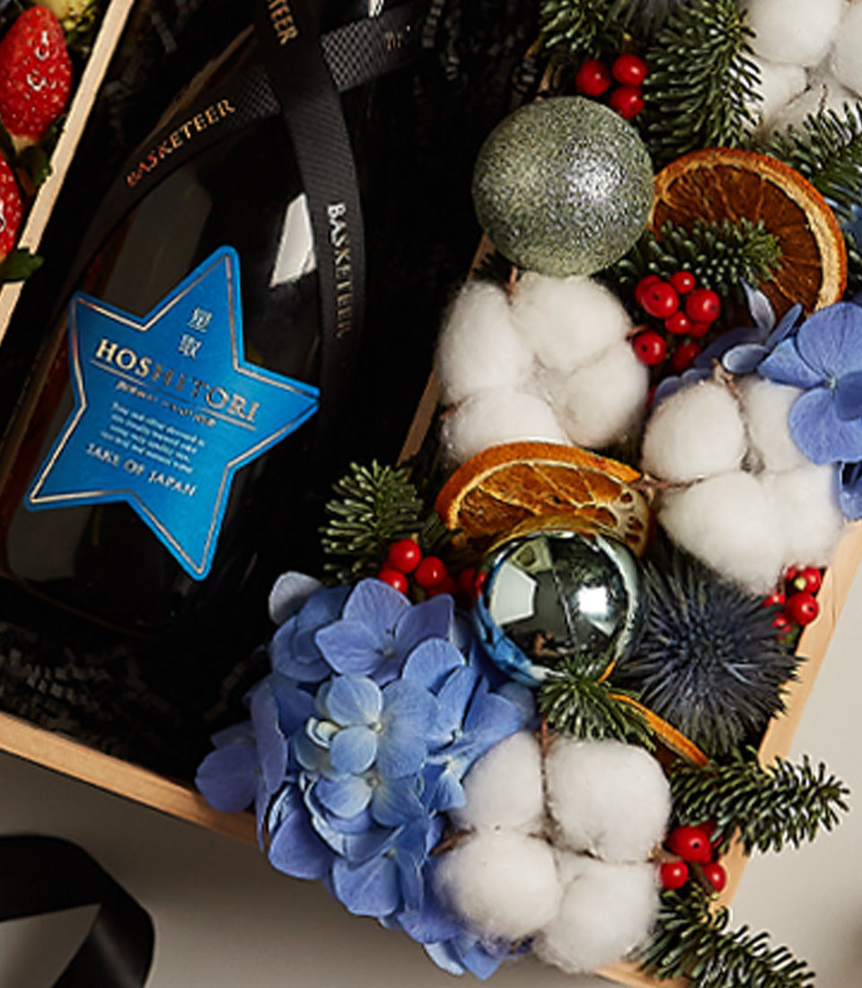 Festive sake gift box with dried citrus, red berries, blue hydrangea, and holiday ornaments in wooden presentation box