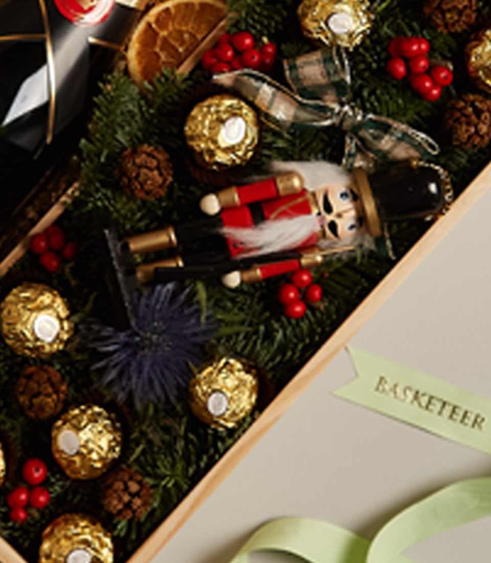 Premium red wine gift hamper with gold-foiled chocolates, nutcracker decoration, and festive holiday trimmings in wooden box