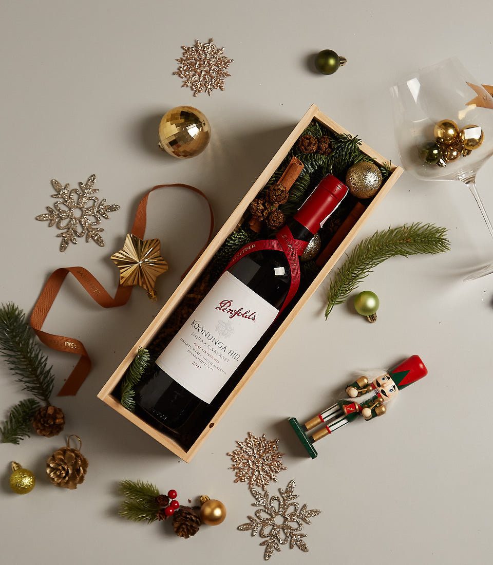 Premium red wine in wooden holiday gift box with pine, cinnamon, and festive gold accents for Christmas gifting