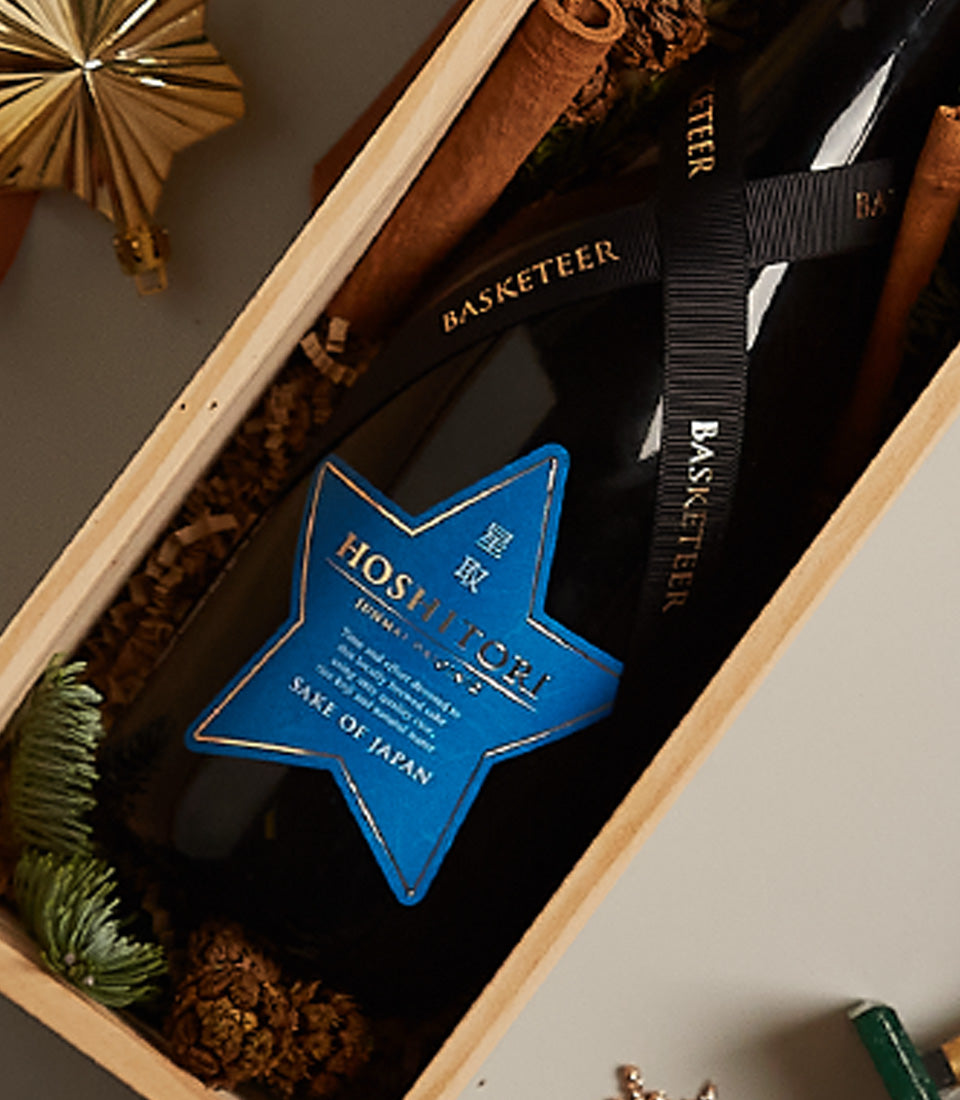 Premium sake gift box with star-labeled Hoshitori bottle, cinnamon stick, and festive woodland accents in light wood