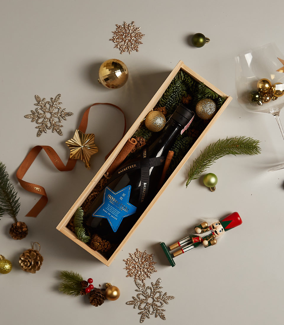 Elegant wooden wine box with Japanese sake, pine branches, cinnamon, and festive gold-and-green holiday ornaments