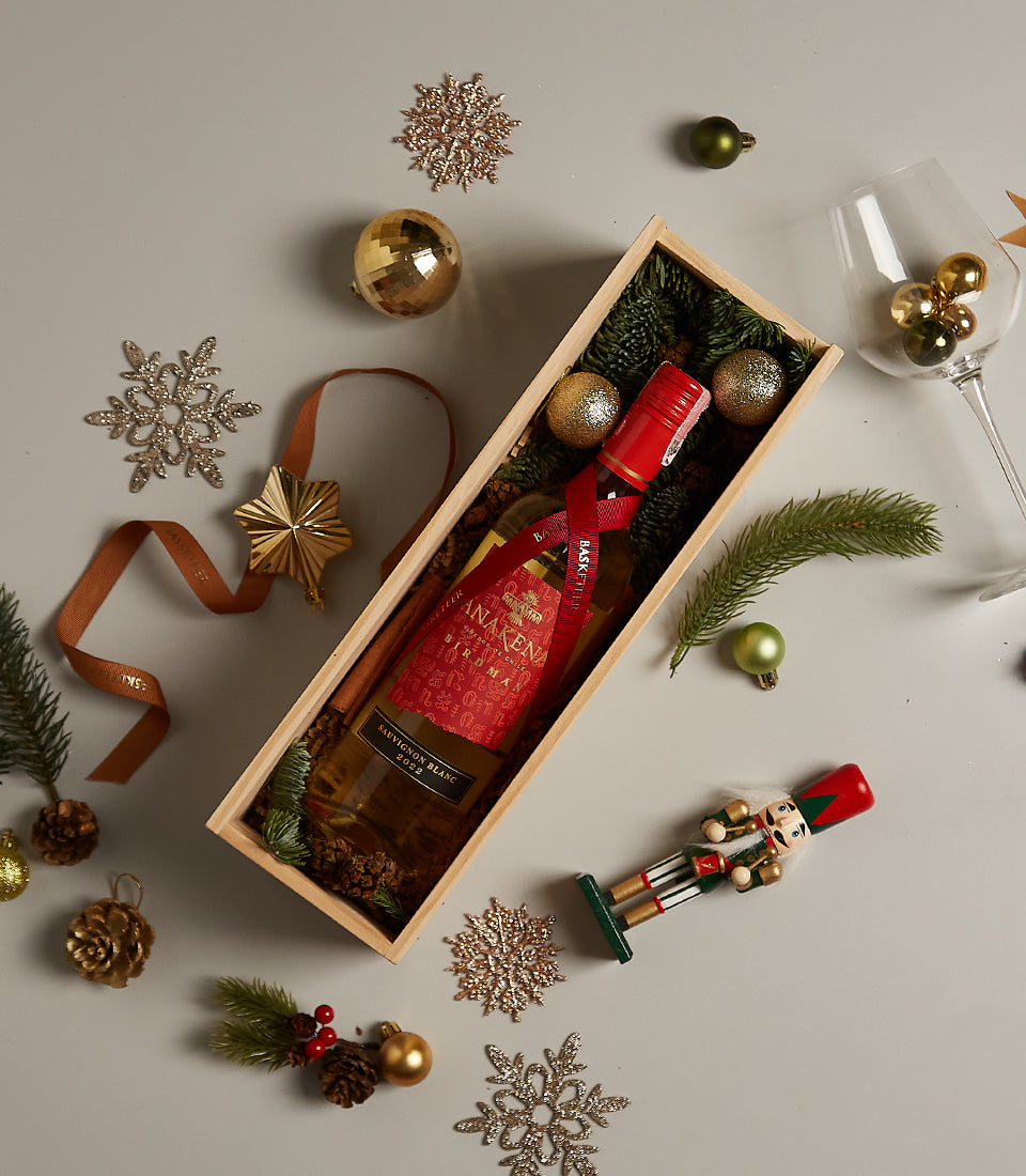 Festive white wine gift box with Anakena Sauvignon Blanc, pine needles, golden ornaments, and red ribbon