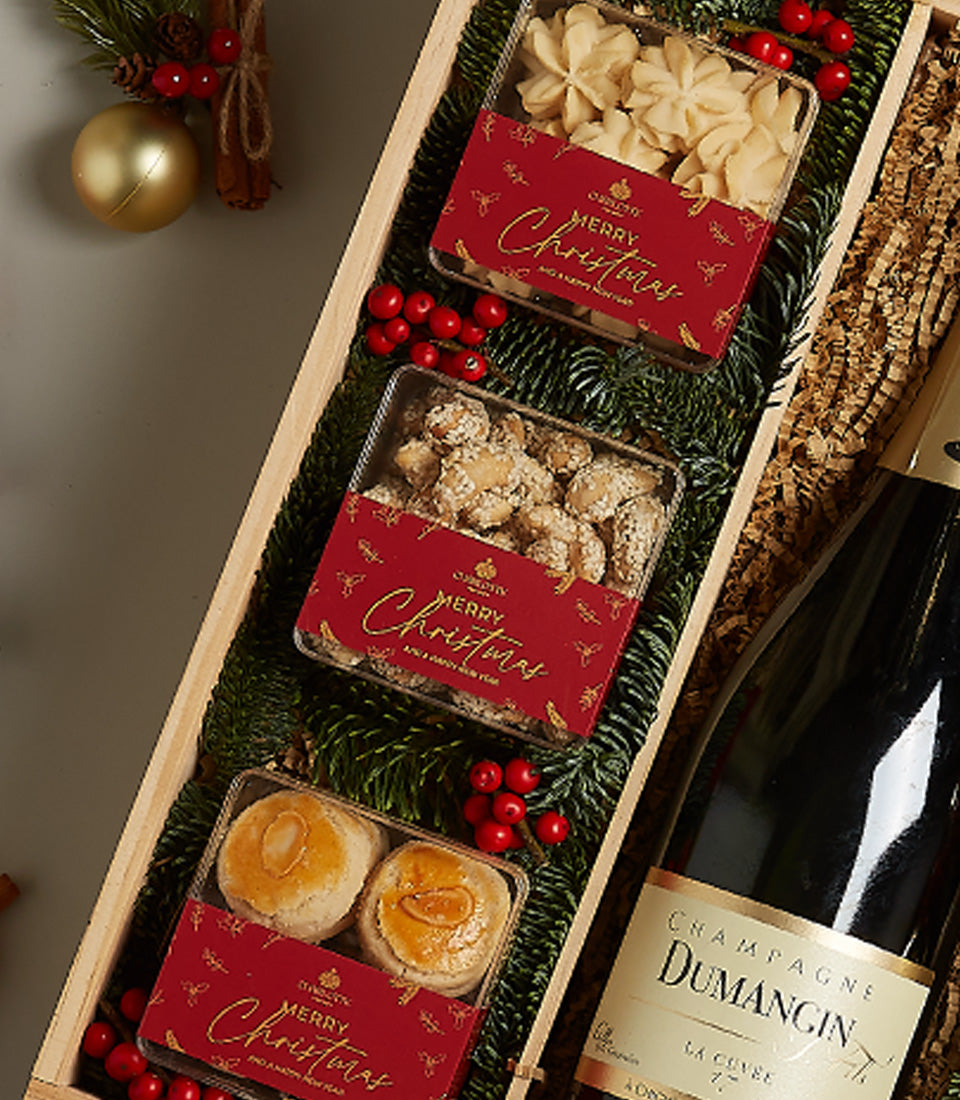 Golden holiday gift box with champagne, star cookies, sugared nuts, and glazed pastries in festive packaging