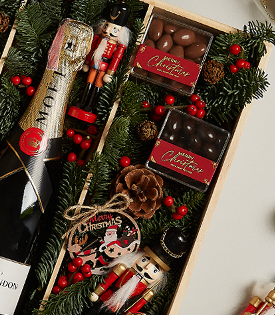 Elegant Christmas gift box with champagne, gourmet chocolates, nutcrackers, and festive pine greenery