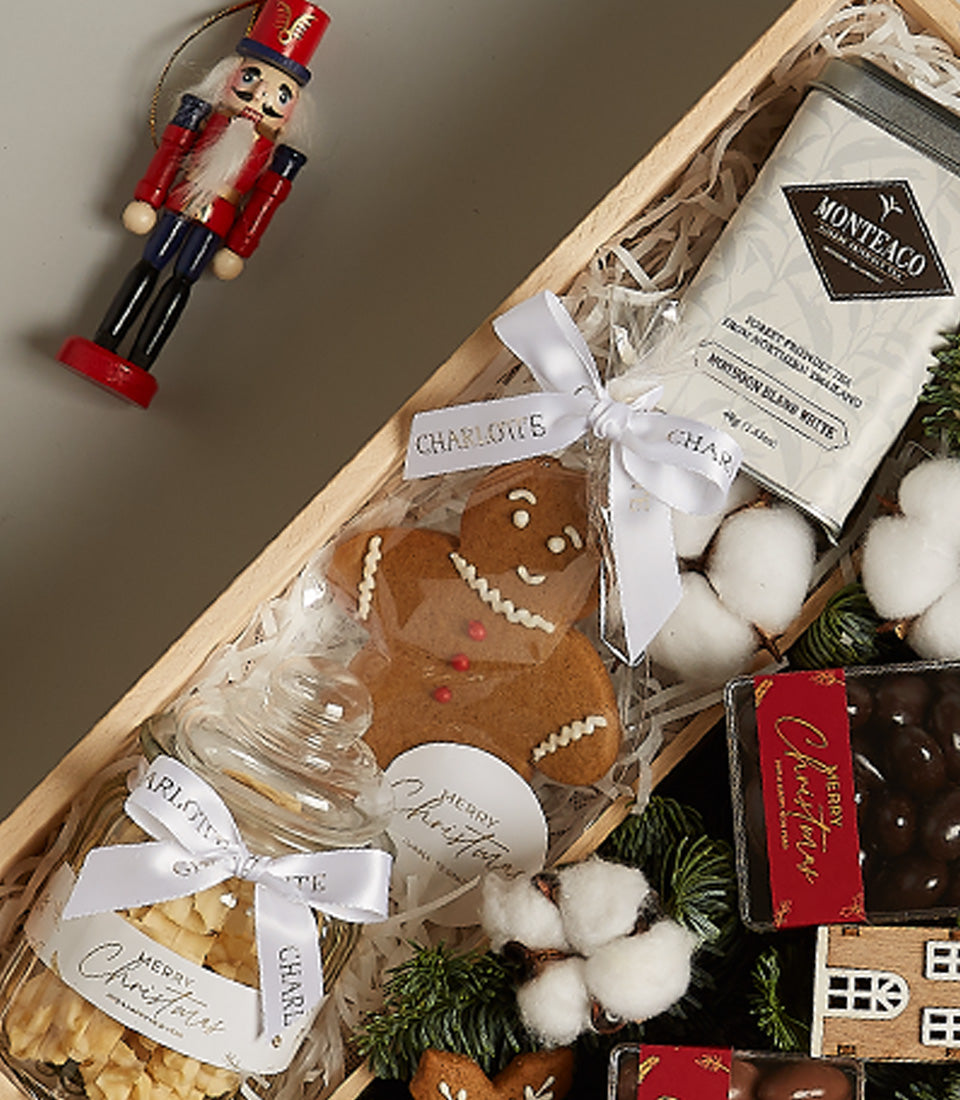 Wooden Christmas hamper with gingerbread cookie, festive tea tin, chocolate truffles, and nutcracker ornament