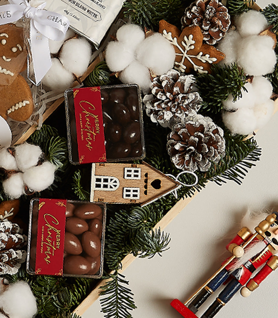 Festive Christmas gift basket with chocolate candies, gingerbread cookies, pinecones, and nutcracker decoration in wooden