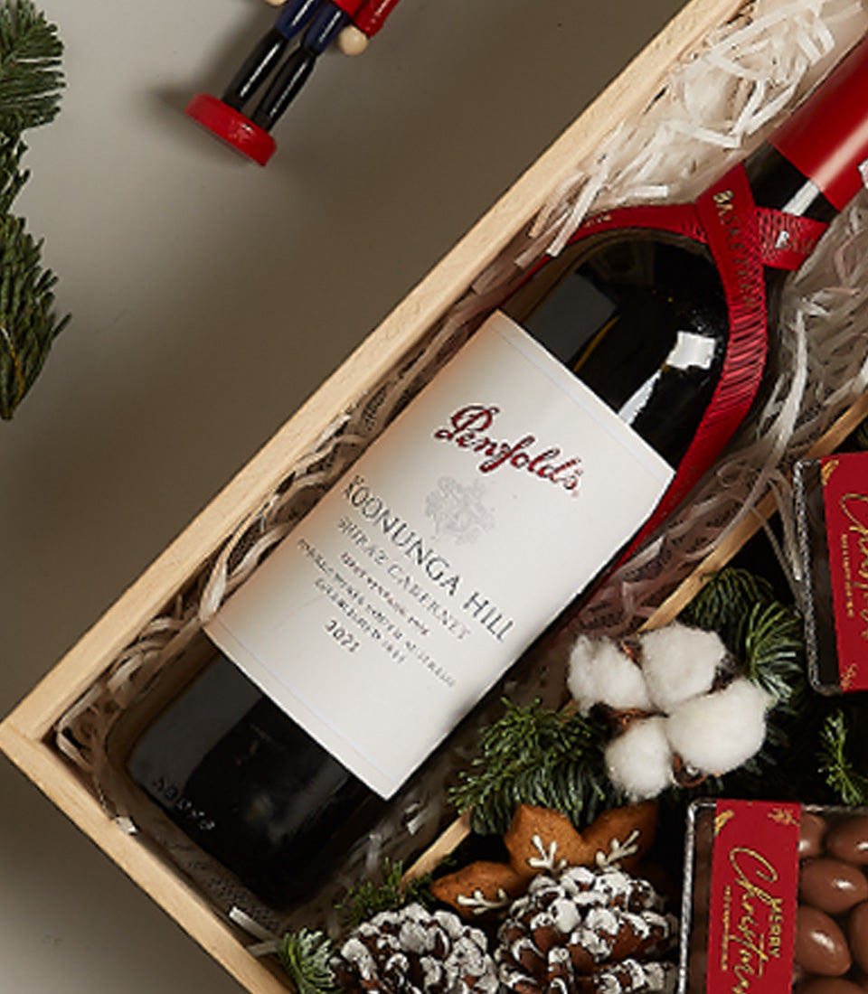 Elegant Christmas wine hamper with red Shiraz, gingerbread cookies, chocolates, and festive natural decorations in wooden