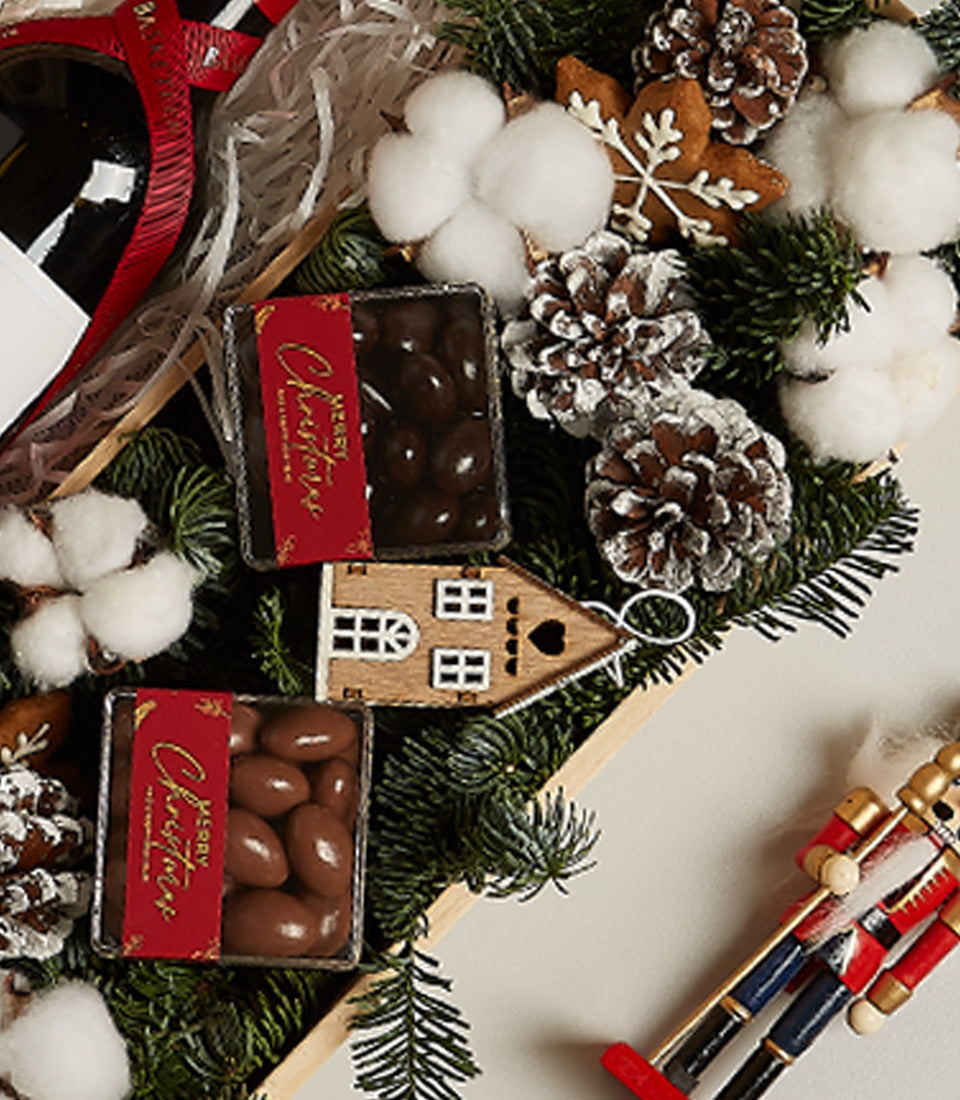 Elegant Christmas wine and gourmet treats hamper with chocolate confections, festive pinecones, and holiday ornaments in