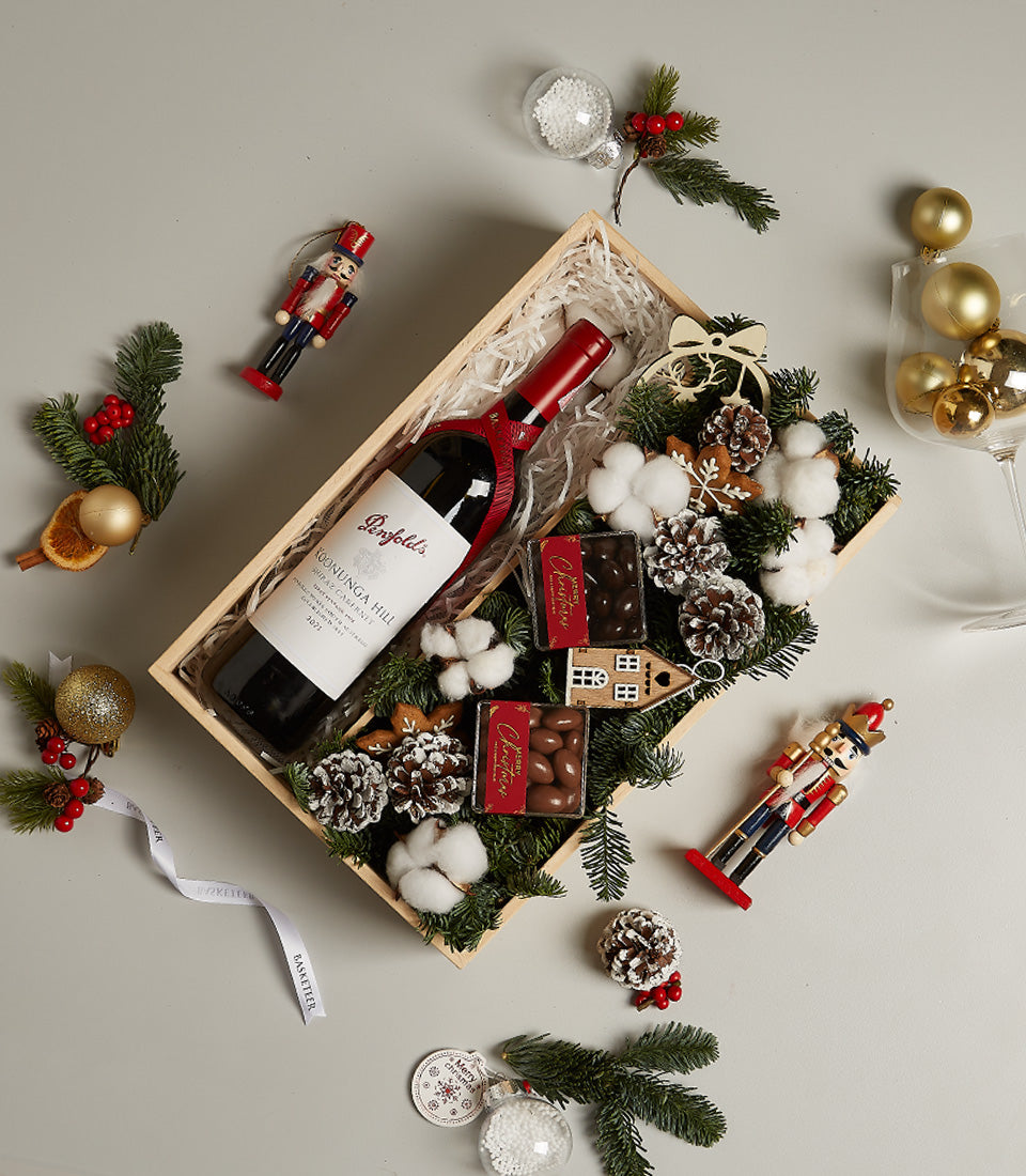 Elegant red wine hamper with gourmet chocolates, frosted pinecones, and festive Christmas decorations in wooden gift box
