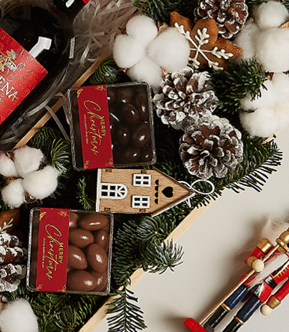 Festive red wine Christmas gift box with chocolate-covered nuts, pinecones, and wooden ornaments in wooden tray