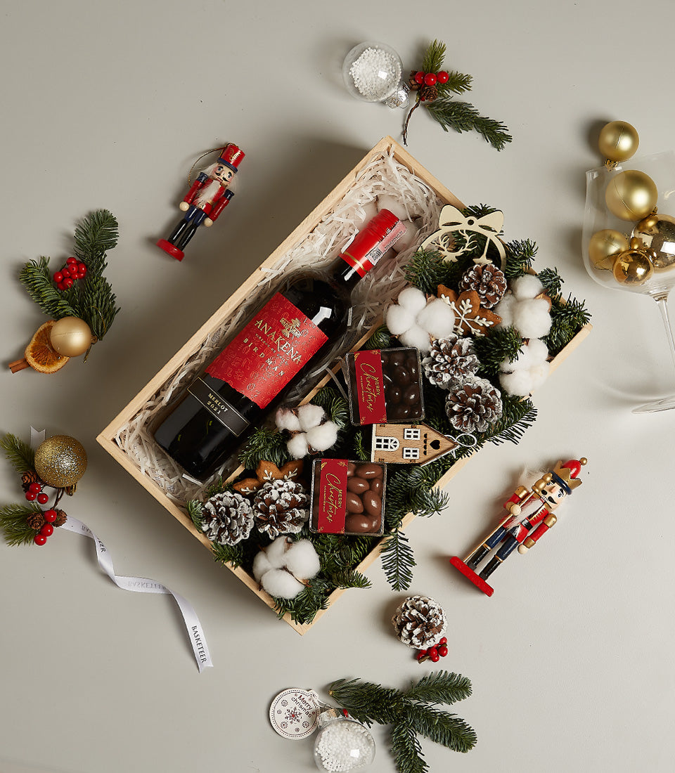 Premium red wine Christmas gift box with artisan chocolates, frosted pine, and festive decorations