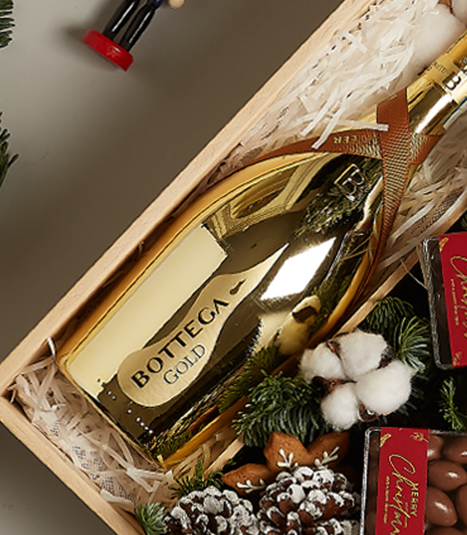 Gold Bottega prosecco with gingerbread stars, frosted pine, and chocolate treats in wooden holiday gift crate