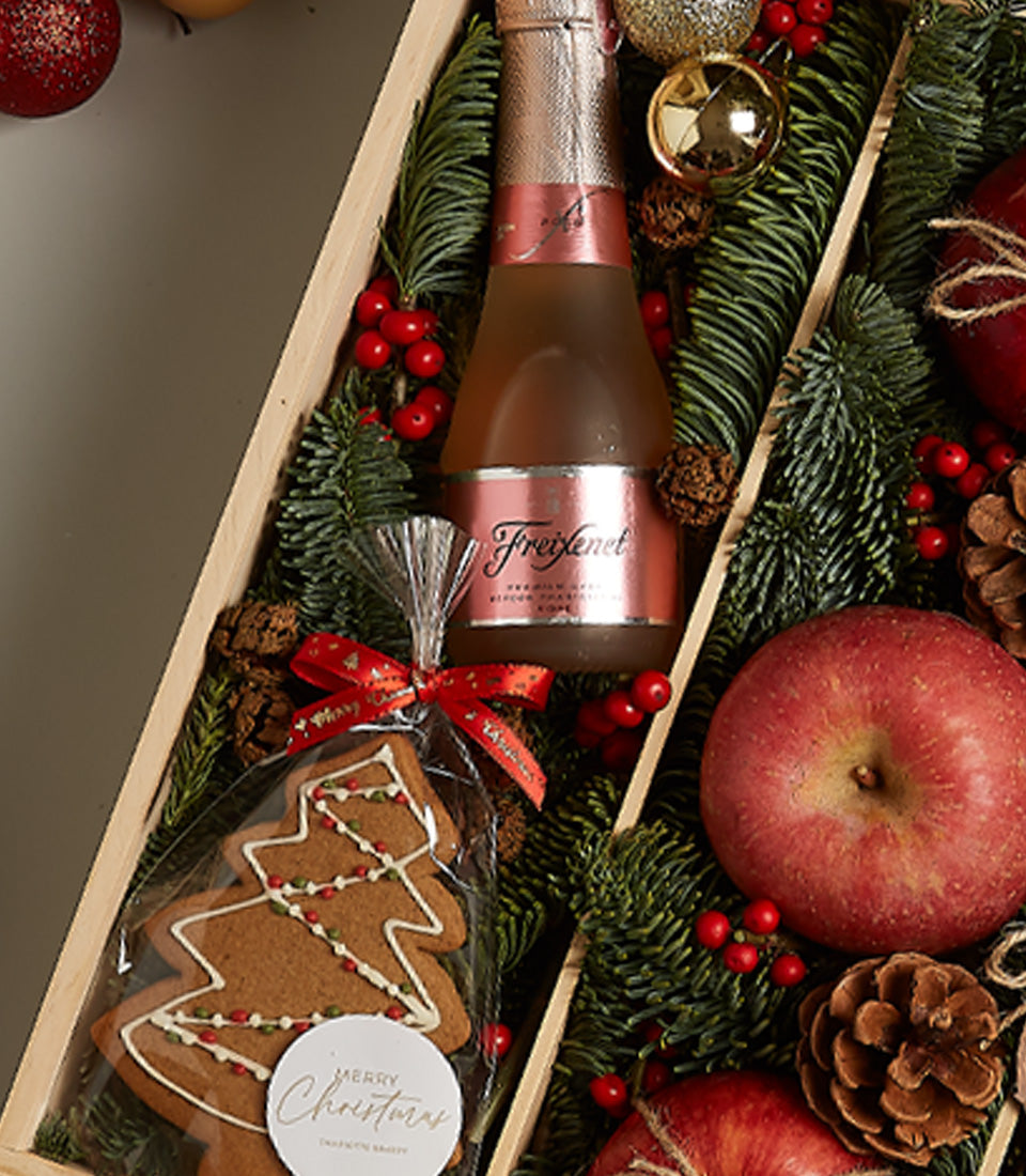 Rosé sparkling wine gift box with gingerbread tree, fresh apples, and festive evergreen for Christmas