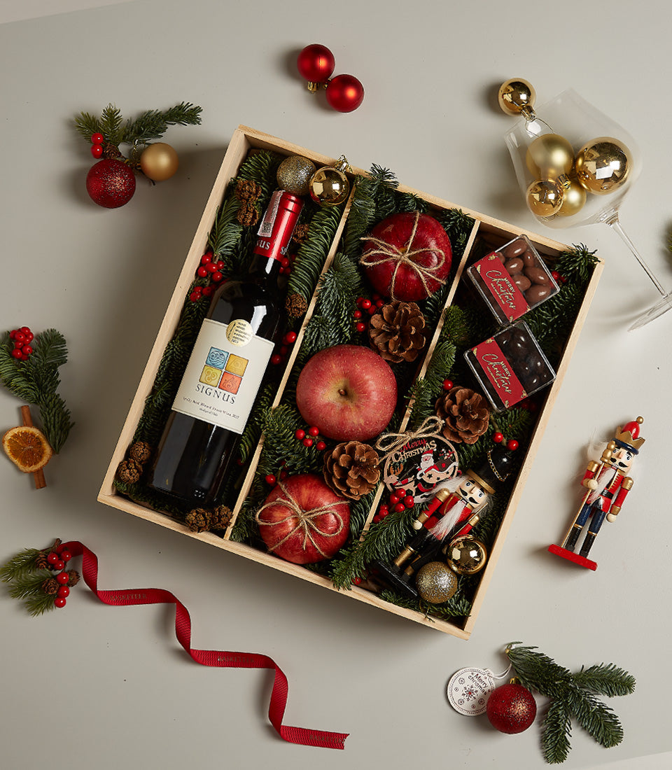 Festive red wine gift box with apples, chocolates, and Christmas decorations in wooden crate