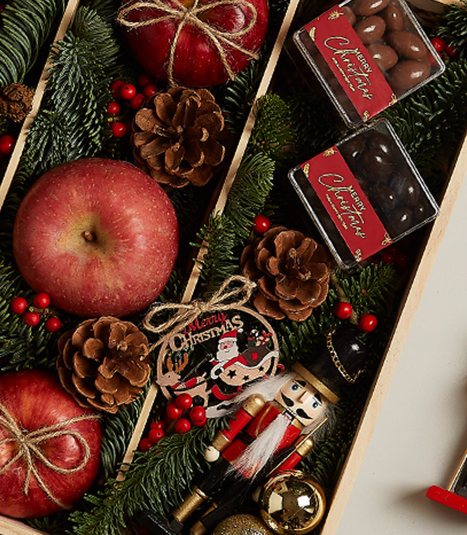 Festive Christmas gift set with Floralba Prosecco, red apples, pine branches, nutcracker, and holiday baubles