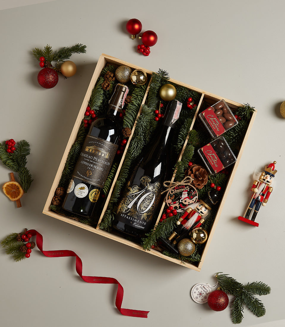 Wooden wine gift box with red wines, chocolates, and festive Christmas ornaments in gold and red