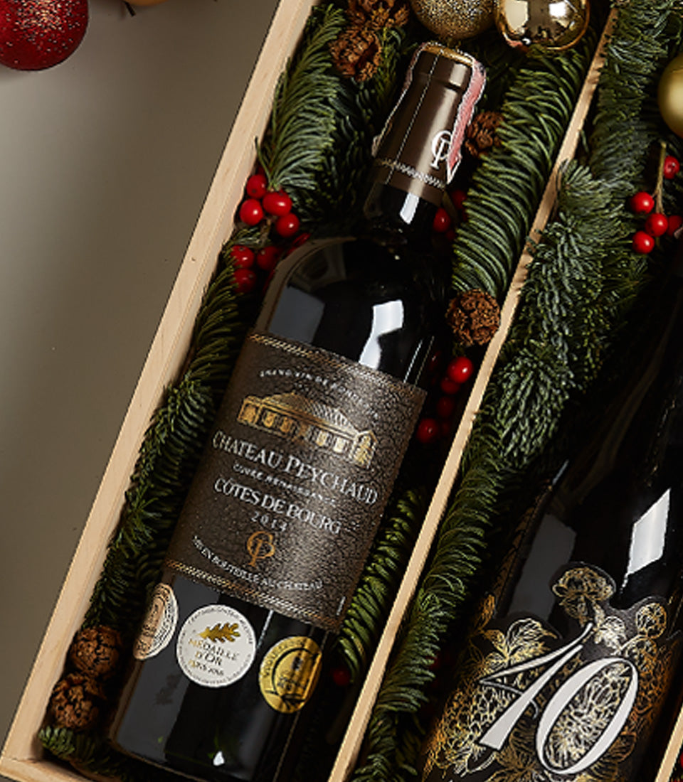 Premium wine and chocolate holiday gift box with Château Peychaud red wine, pine branches, and festive berries
