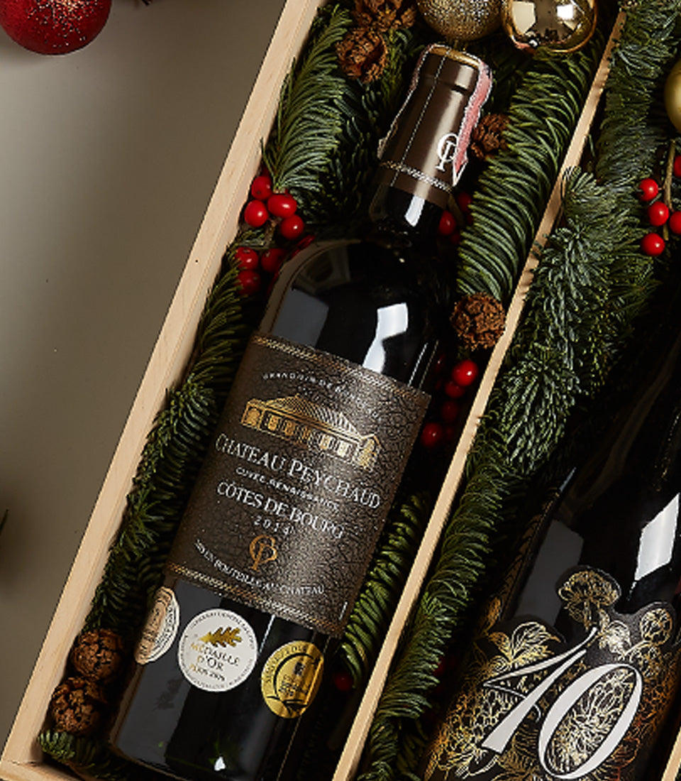 Elegant wine hamper with two premium red wines, festive greenery, berries, and pine cones in wooden gift box